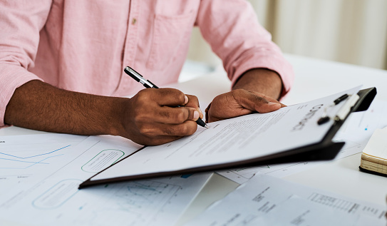 Closeup shot of an unrecognisable businessman filling in paperwork in an office